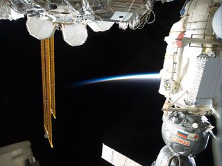 A docked Russian Soyuz spacecraft (right) backdropped by the thin line of Earth's atmosphere and the blackness of space is featured in this image, which was taken by the STS-133 crew. The image also features a portion of the International Space Station's