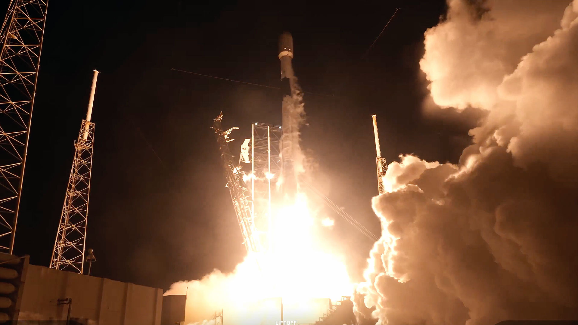 a white and black rocket launches into the night, its orange and white engine plume lighting the ground below