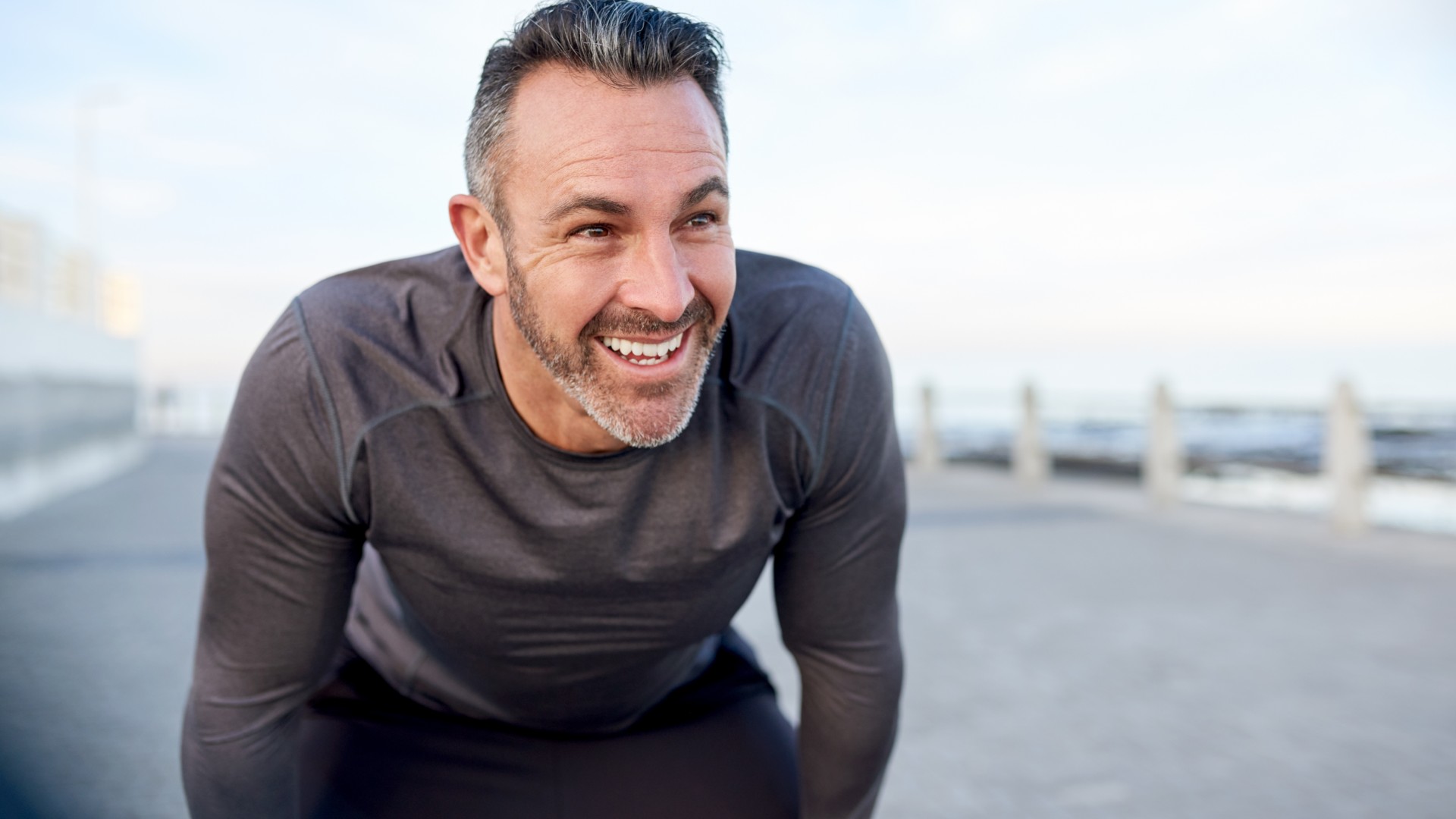 Male smiling to camera outdoors with hands on knees 