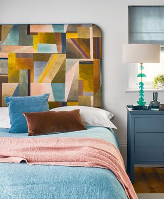 A large headboard with a colorful, abstract pattern on a bed with blue bedding