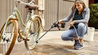 A woman using a worx pressure washer to clean her muddy bike 