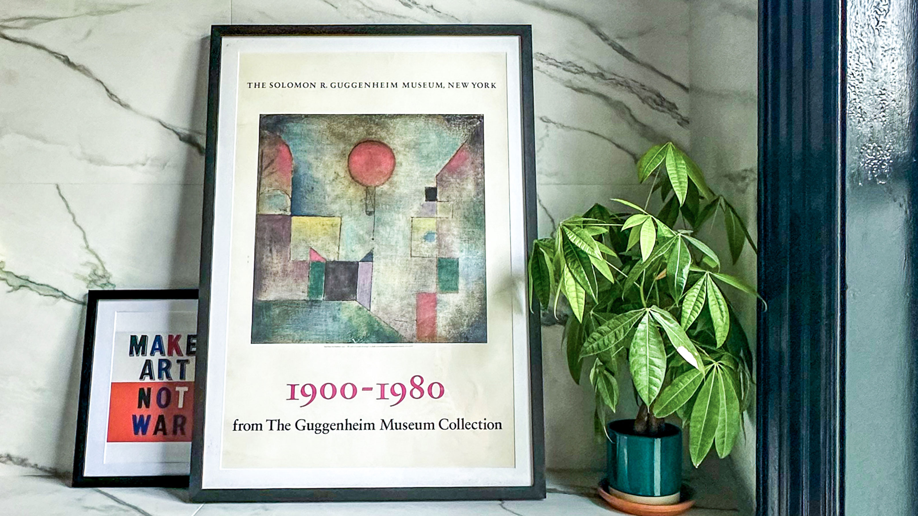 Pot plant and two framed artworks on ledge in marble bathroom