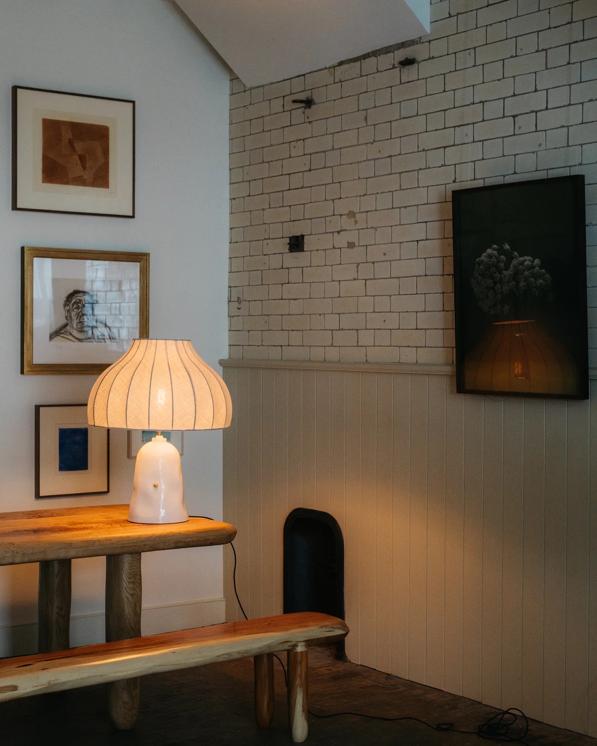 Image of the corner of a room with a wooden dining table and a matching wooden bench. There is a glossy white mushroom lamp.