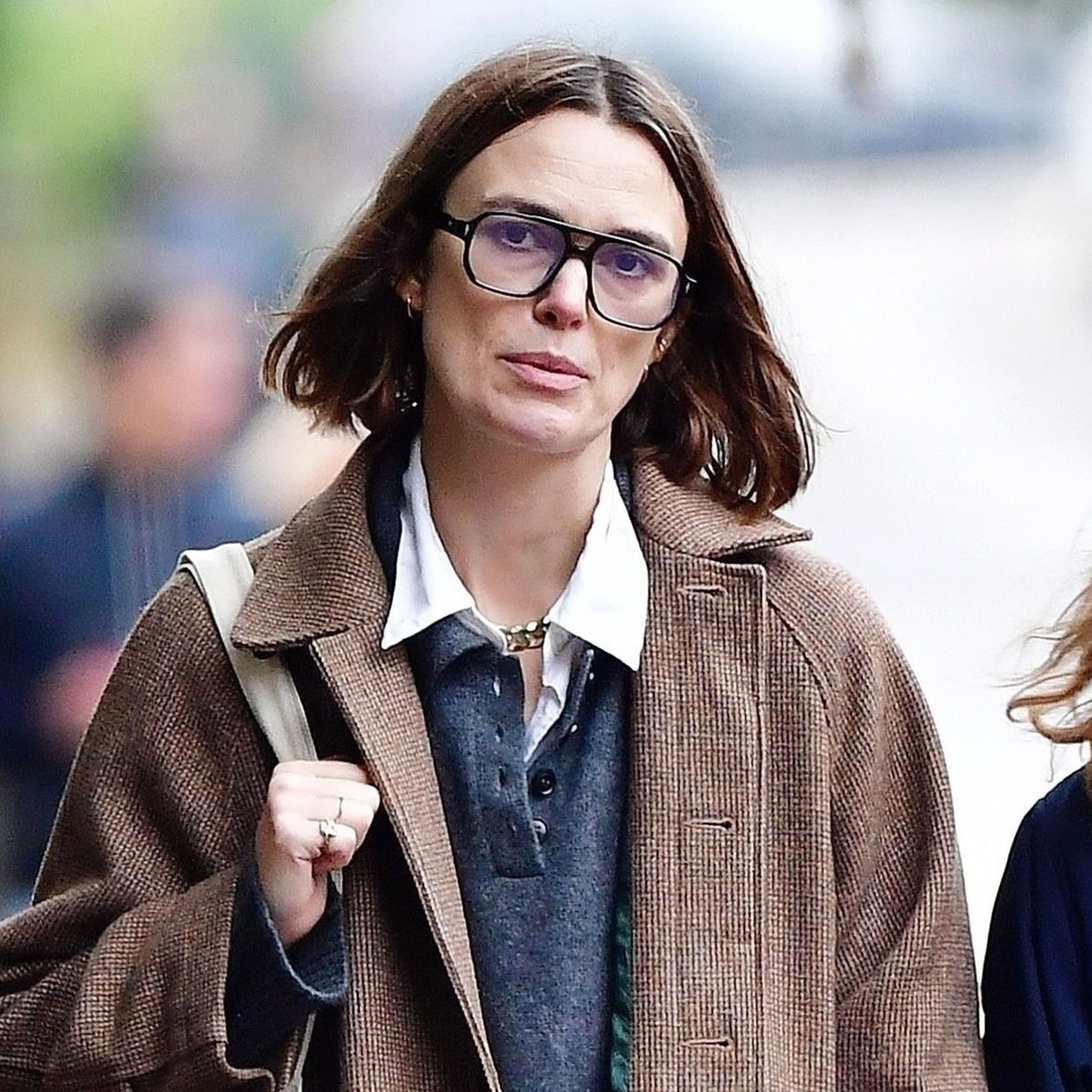 Kiera Knightly wearing a brown coat, navy polo, darkwash jeans, and black 