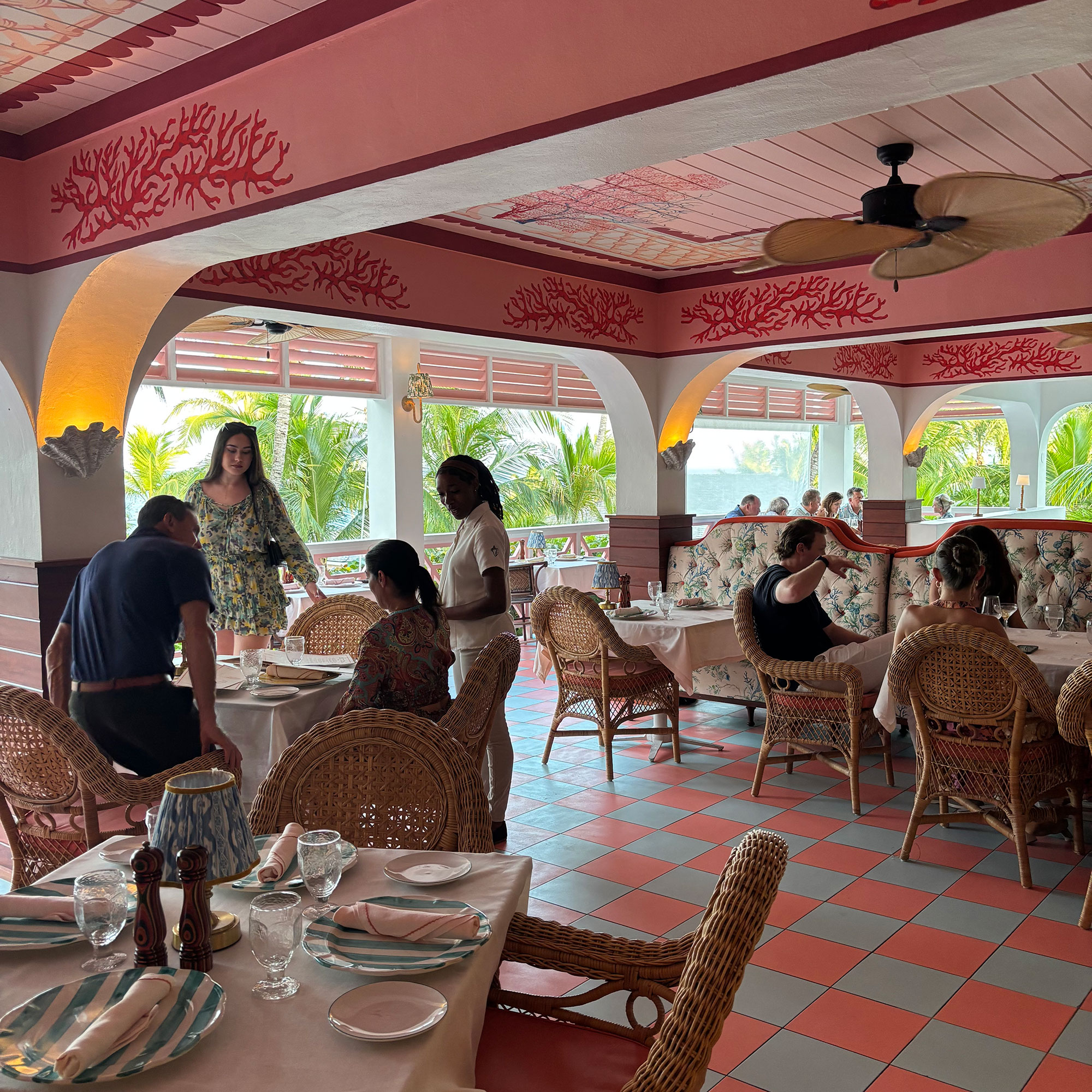 Restaurant with pink and turquoise tiled floor, wicker dining chairs and ceiling painted pink with coral motifs