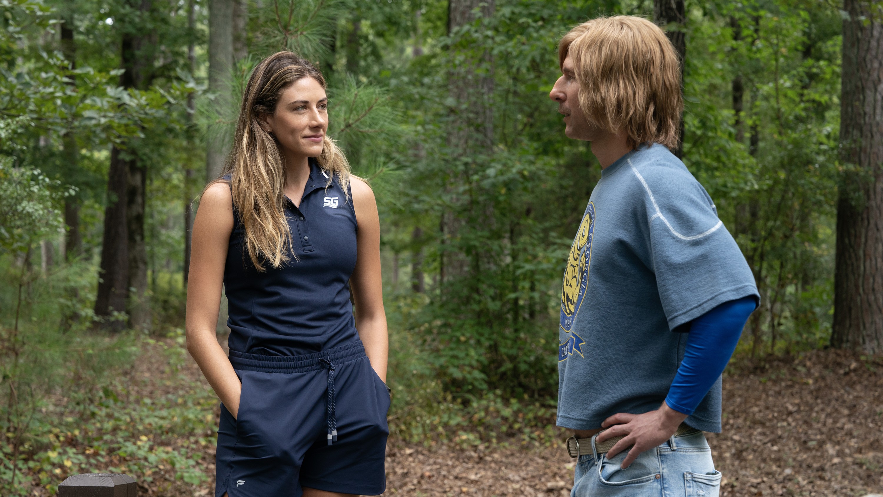 Perry Mattfeld and Glen Powell standing in the woods in a still from the Disney+ show Chad Powers