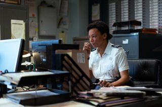 Leigh (Nina Sosanya) sits at the computer in her office in the prison. Her left hand is moving the house, and her right hand is up in front of her face. She is leaning toward the monitor and looks concerned.