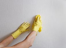 Cleaning white wallpaper while wearing rubber gloves