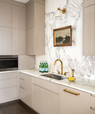 kitchen with sleek plaster colored cabinets and marble backsplash and painting above sink