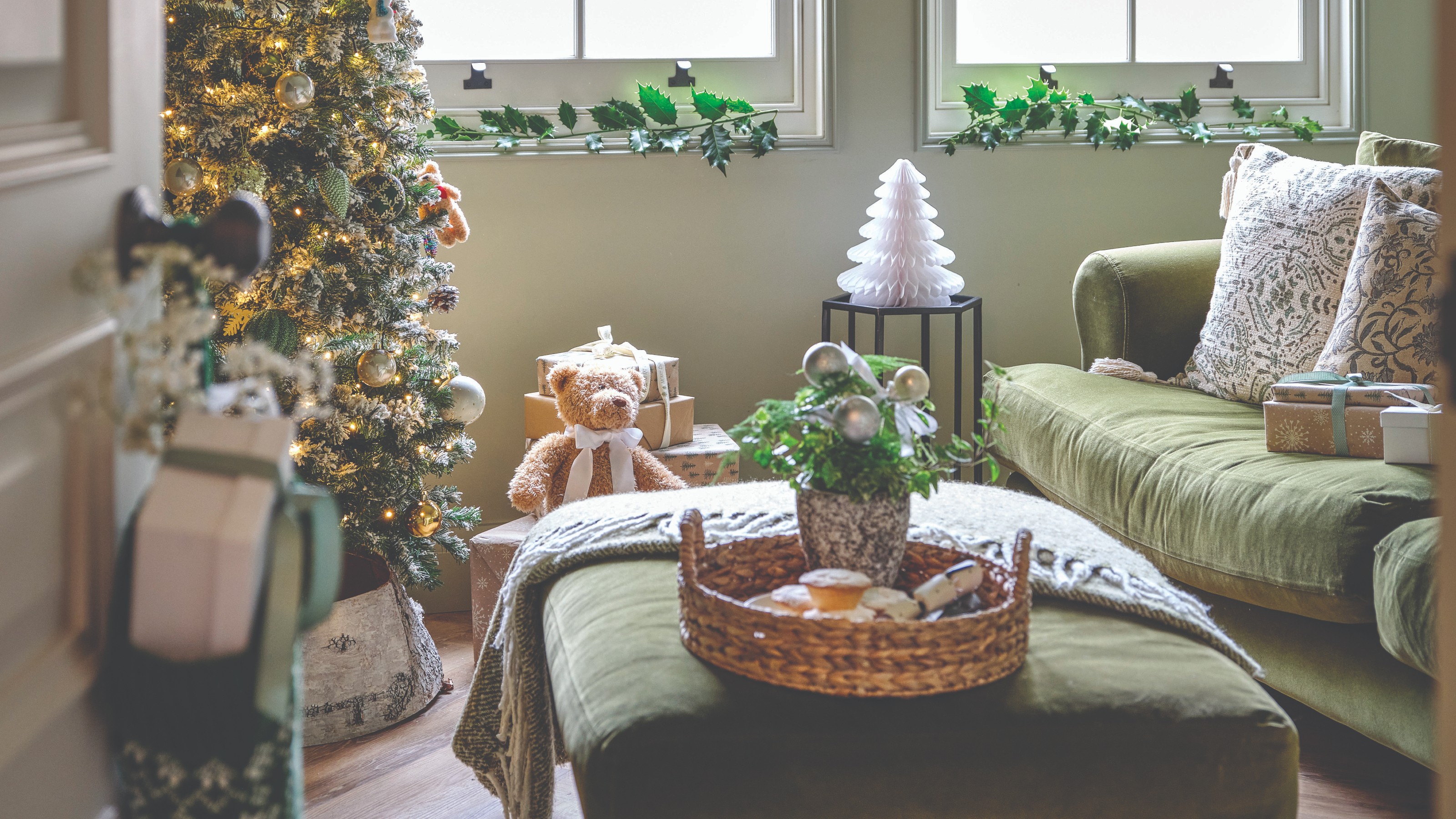 A living room with green velvet sofa and ottoman decorated for Christmas with a slim tree