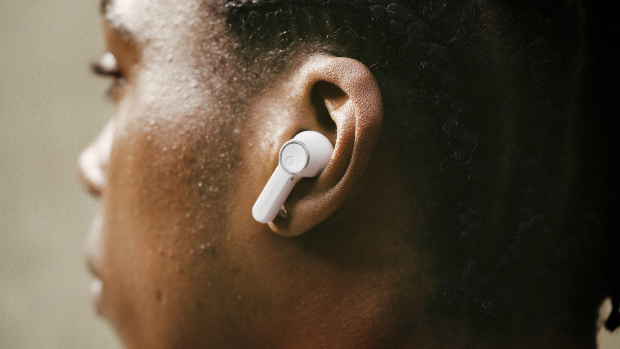 A young man with black hair wearing Cambridge Audio Melomania A100 earbuds in white