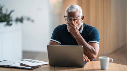 Stressed man in front of laptop rubs his eyes