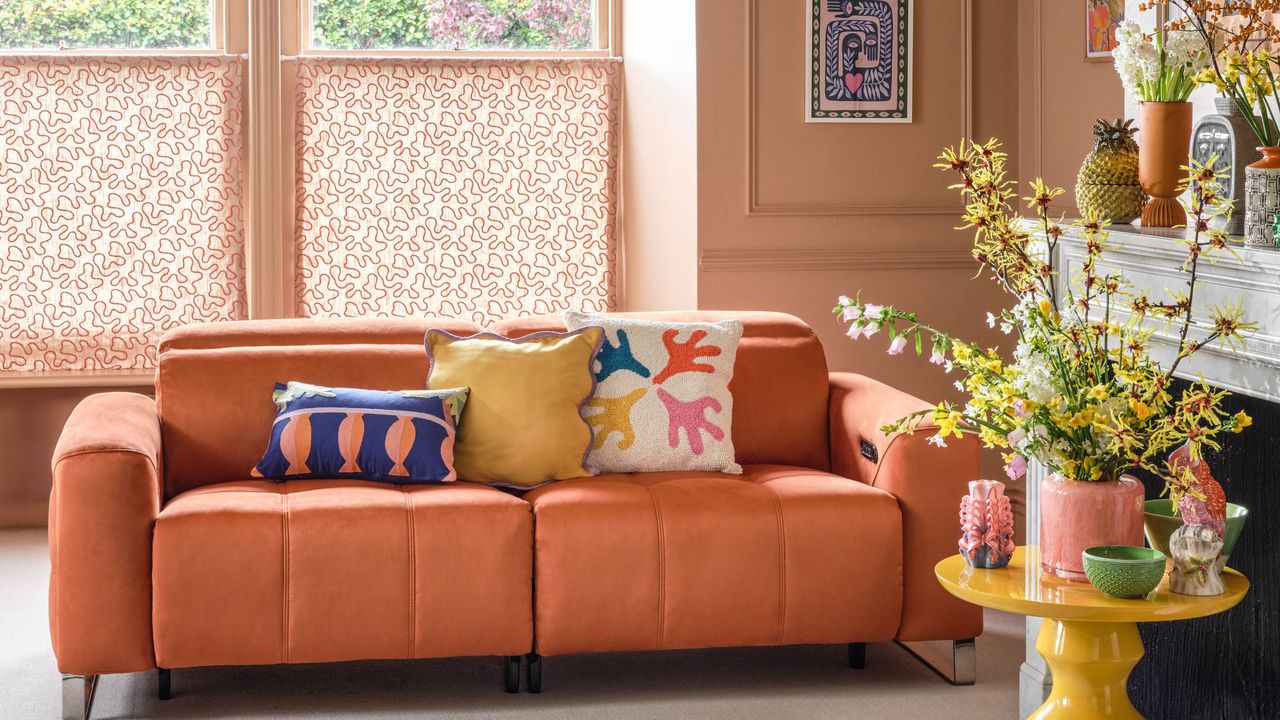 A small living room with peach walls and a peach couch with colorful cushions