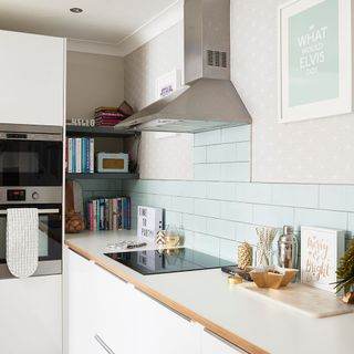 kitchen with white counter tiles and wallpaper on wall and exhaust system