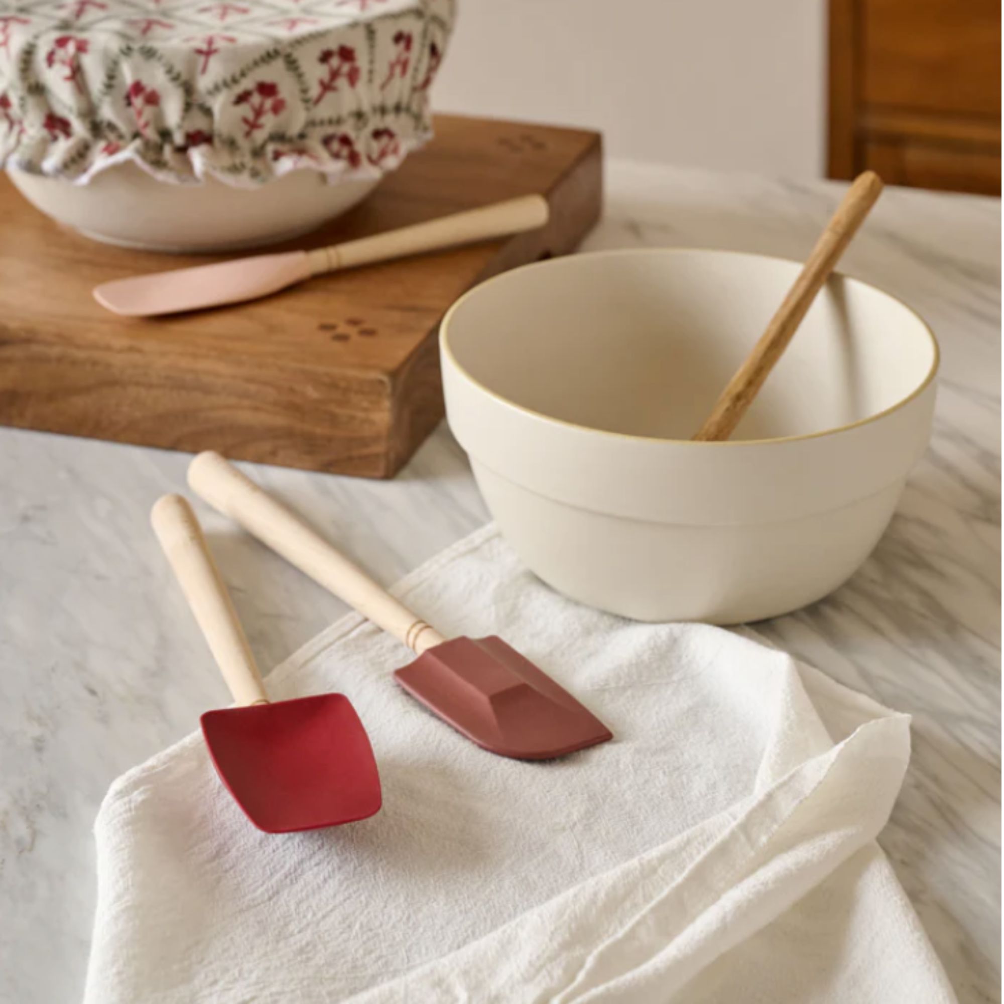 White mixing bowl and red spatulas on a white marble countertop