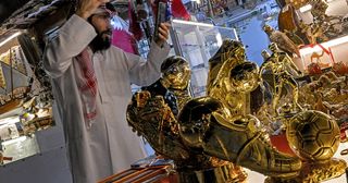 A merchant uses a phone to check his styling as he stands before golden boot trophy replicas and other memorabilia at the Souq Waqif market in Doha on December 1, 2022, during the Qatar 2022 FIFA World Cup football tournament.