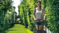 a woman using one of the best electric lawn mower options in her garden in the sun