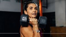 Woman holding up 12kg dumbbell in one hand, looking at camera, doing strength training for women