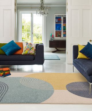 Punchy, large scale geometric rug zoning blue sofas with multi-colored scatter pillows.