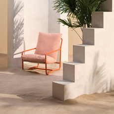 John Lewis Marcy Sling chair in burnt office on a beach next to a stone building and wall.