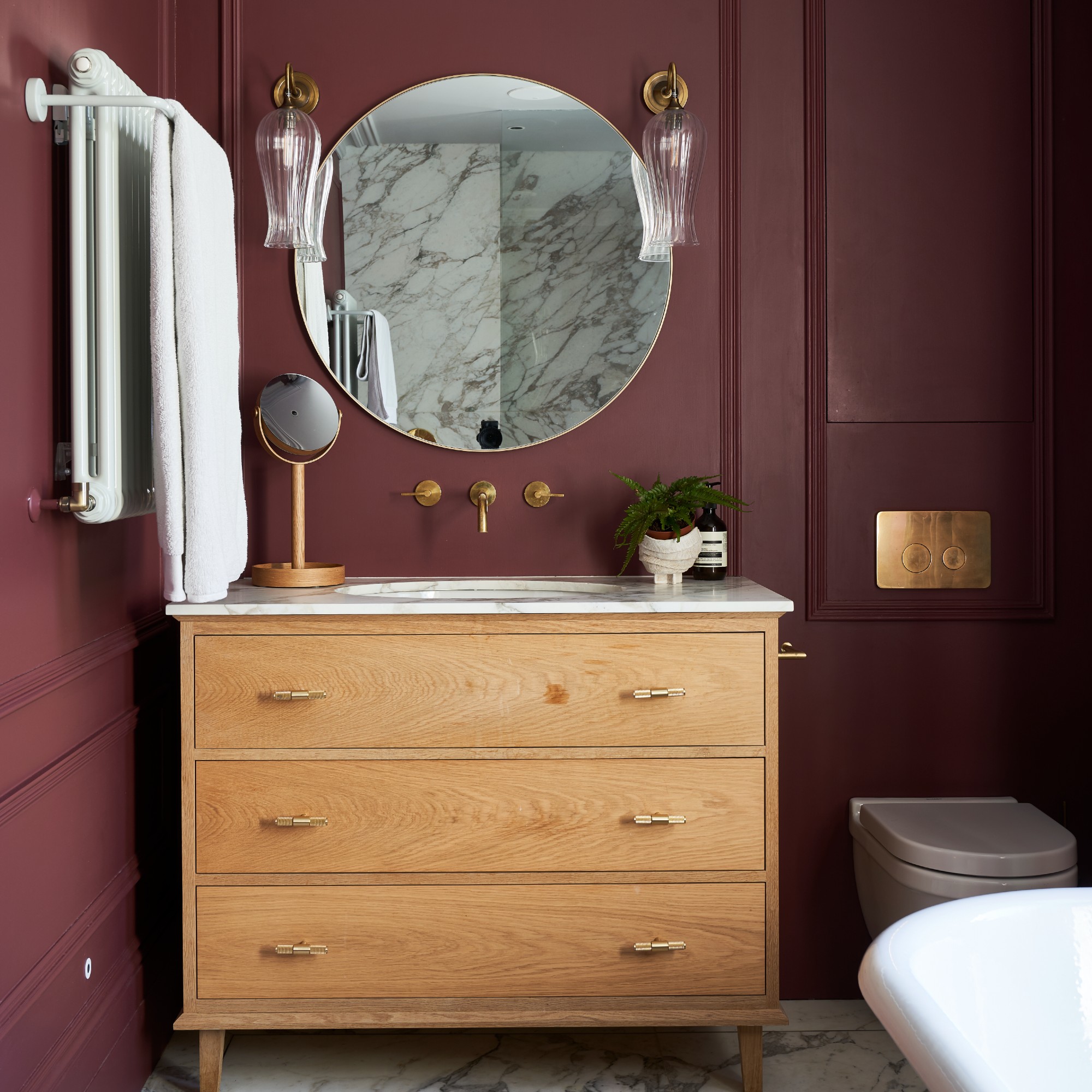 A purple-painted bathroom with a round wall mirror above a wooden bathroom cabinet