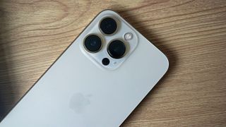En vit iPhone 13 Pro ligger på ett träfärgat bord med baksidan och kameramodulen vänd uppåt.