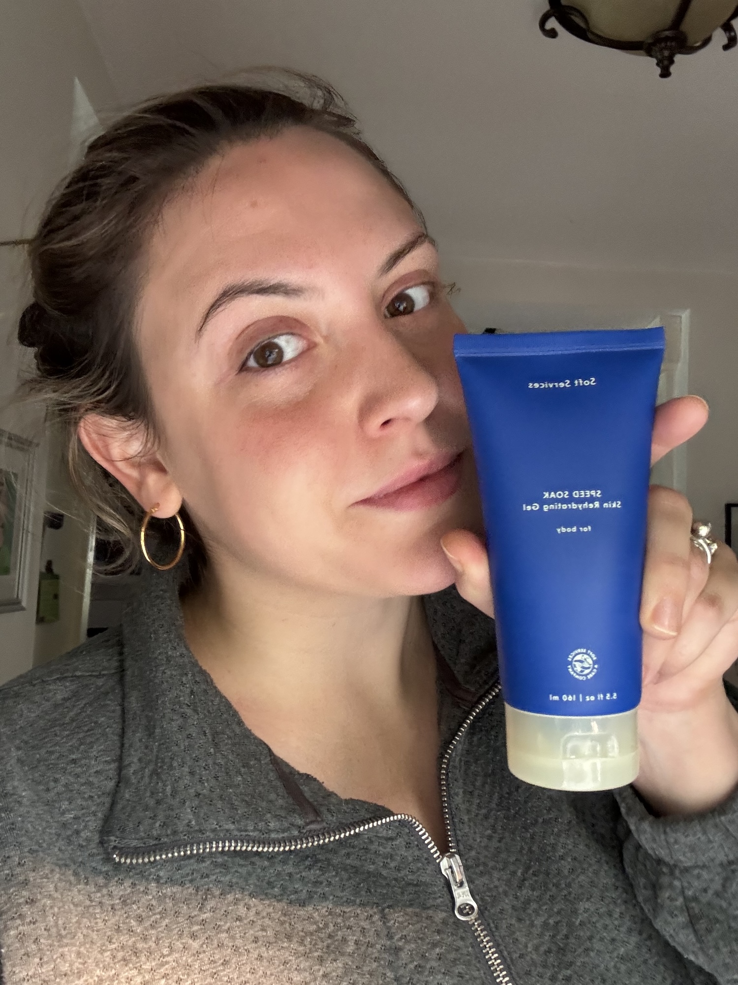 Sophia Vilensky and her bottle of Speed Soak gel moisturizer in a grey zip up sweater.