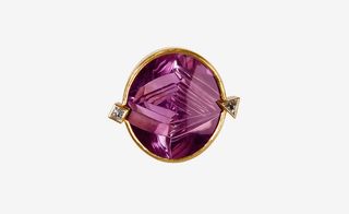 Pink jewel set in a gold ring with a square diamond on one side and triangular one on the other
