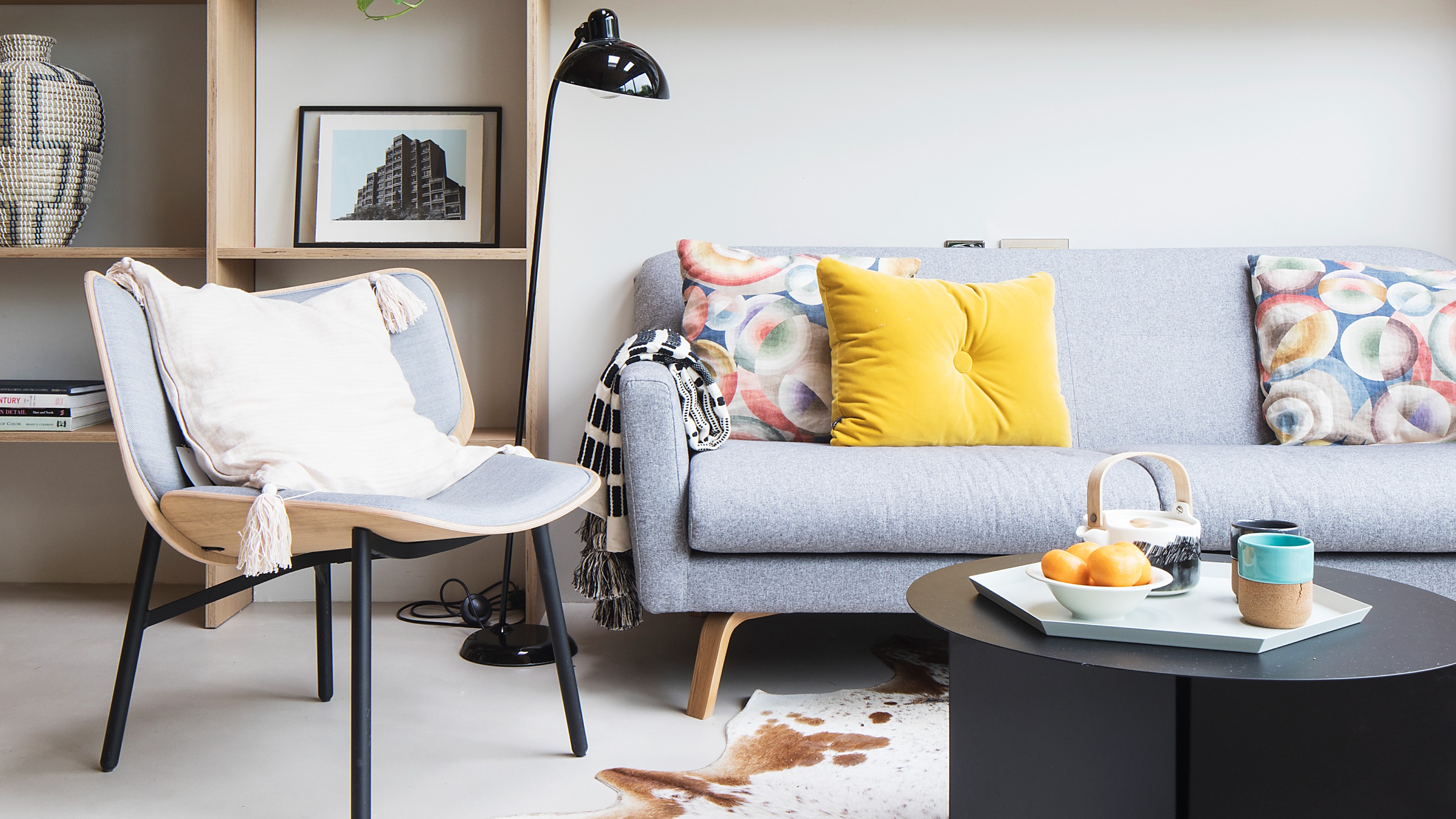 A living room with a grey sofa with colourful scatter cushions, a cow-print rug and a round black coffee table