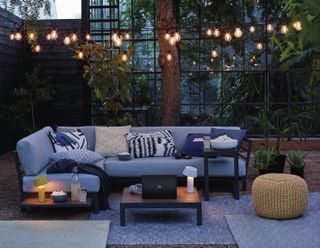 Grey outdoor sofa by John Lewis in an atmospheric terraced area outside, with fairy lights and tables