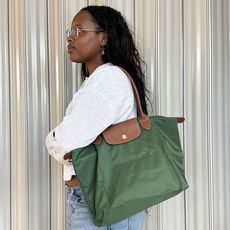 A woman wearing a grey hoodie, blue jeans, and a green canvas tote bag