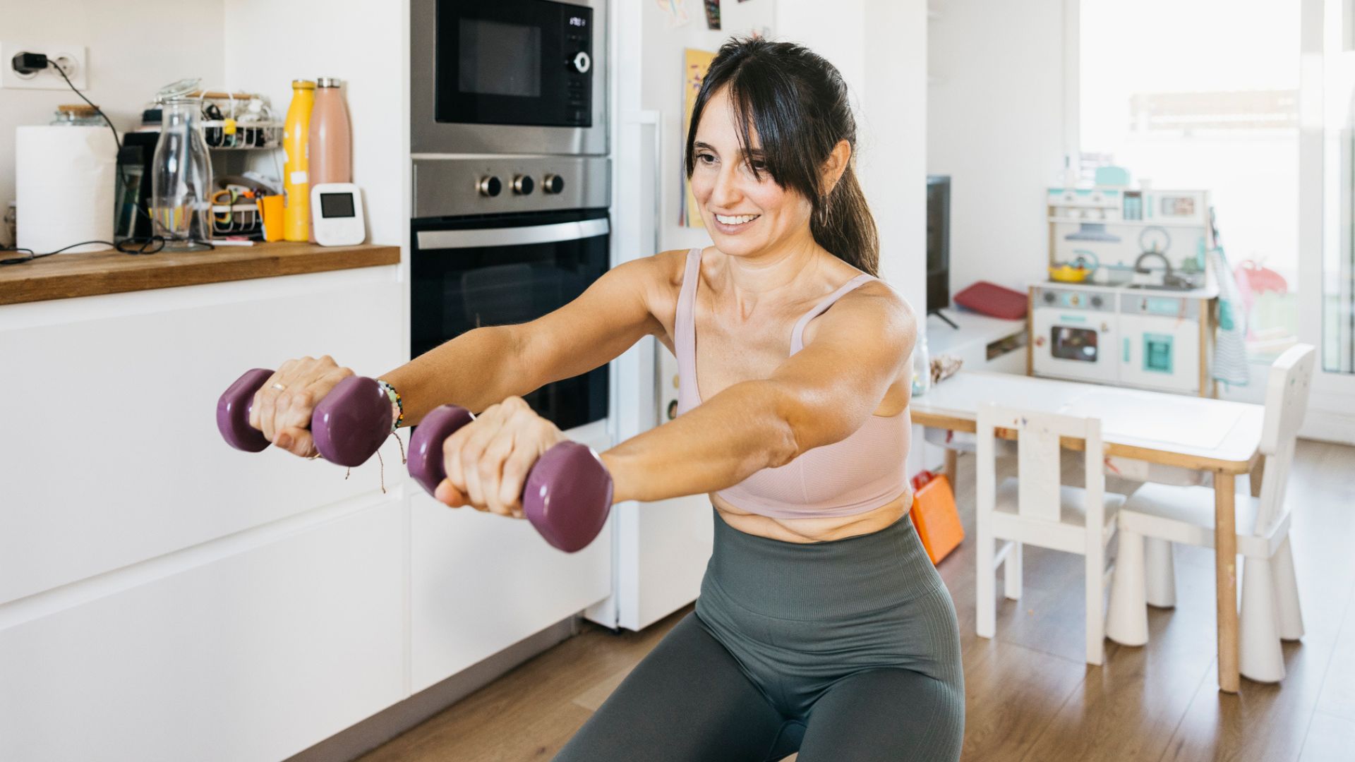 woman works out with dumbbells in her kitchen