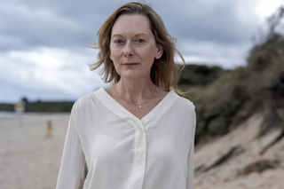 Cathy Belton as Claire Collier, on the beach wearing a white shirt.