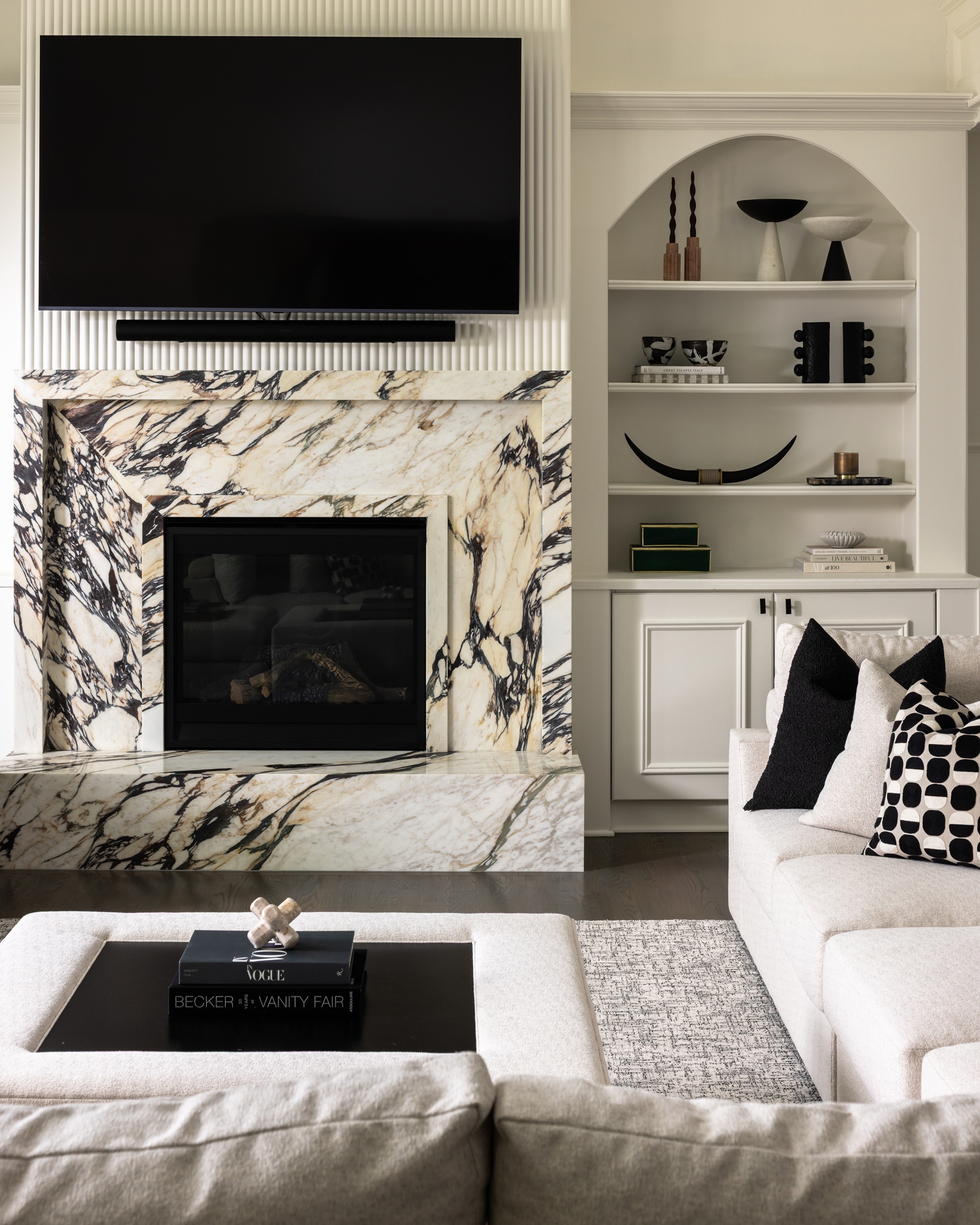 a white living room with a viola fireplace with a tv over the top and shelves to one side