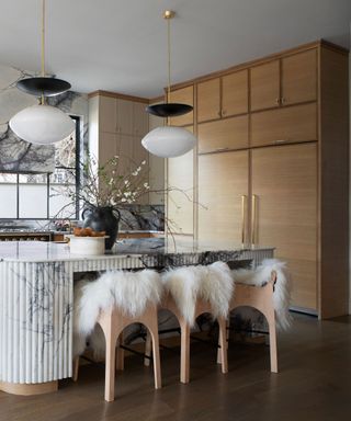 Wooden kitchen with large island and bar chairs topped with faux fur rugs for a cozy, modern finish