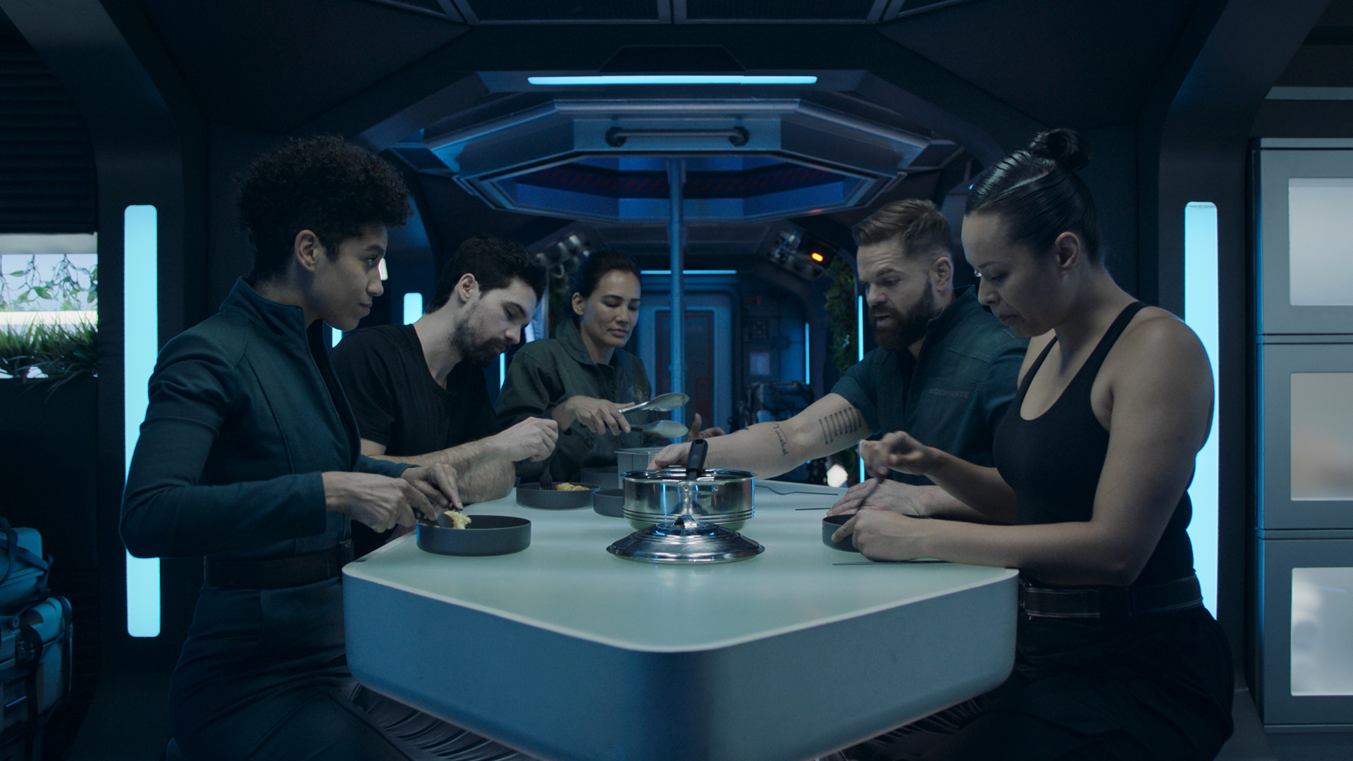 Five people sat at a table eating a meal aboard a spaceship.