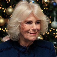 A headshot of Queen Camilla standing in front of a Christmas tree and wearing a blue coat