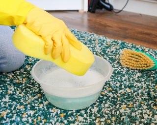 Gloved hand spot testing on carpet with bowl of liquid with dish soap in and sponge