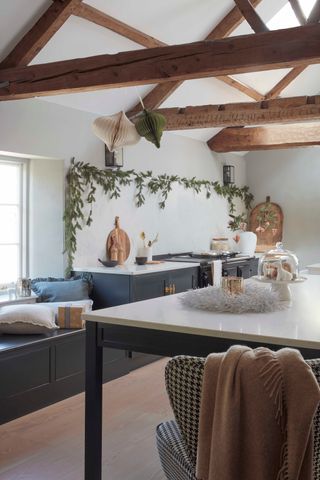 black and white kitchen with beams, kitchen island, white countertops, garland on the wall above the range, two paper Christmas decorations hanging from beam