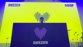 A DJ stands behind a booth with the new Deezer logo on it