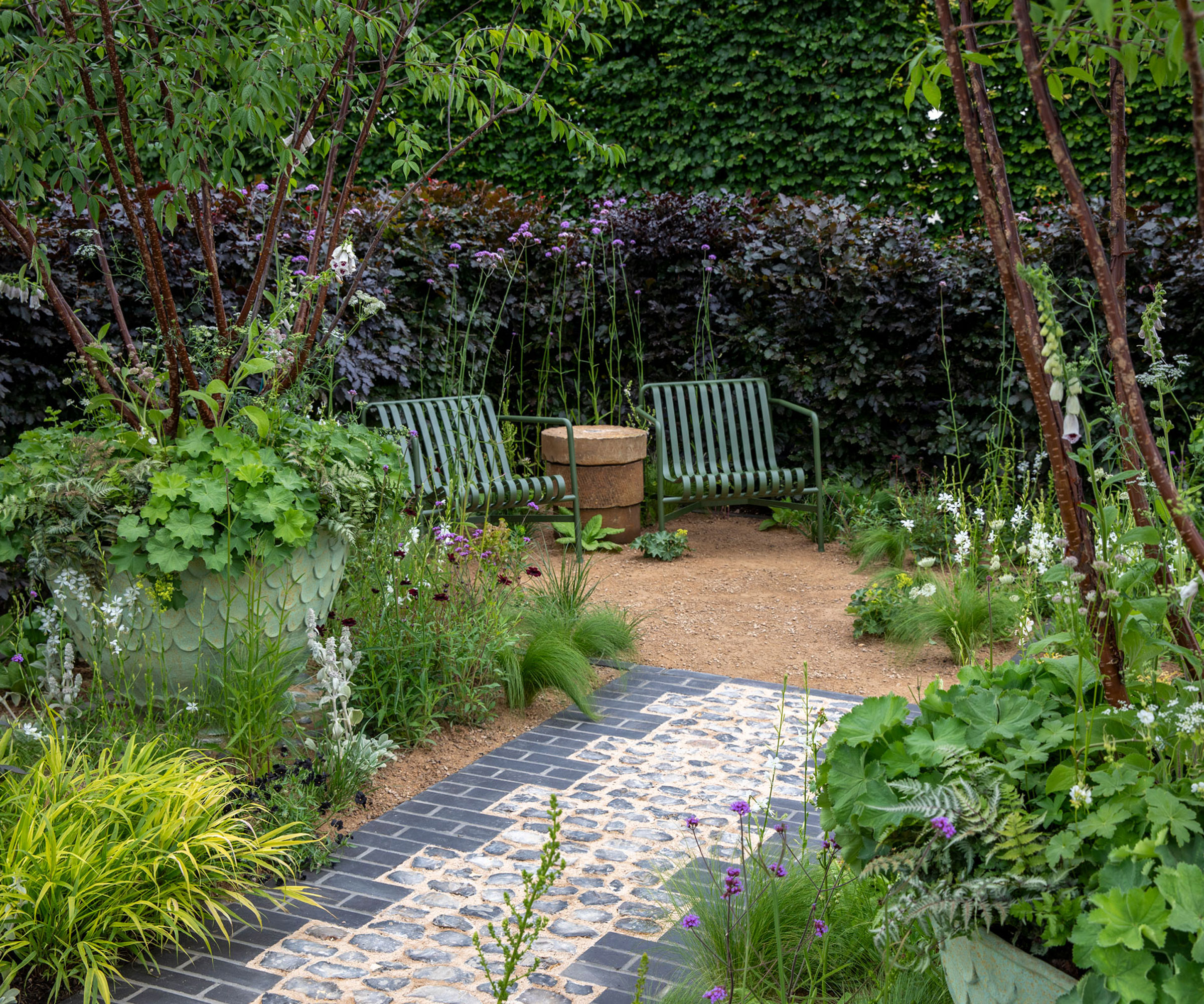 enclosed seating around design surrounded by planting, with garden chairs, gravel landscaping, container gardens and paving