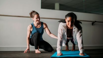 Instructor kneels next to woman holding plank position