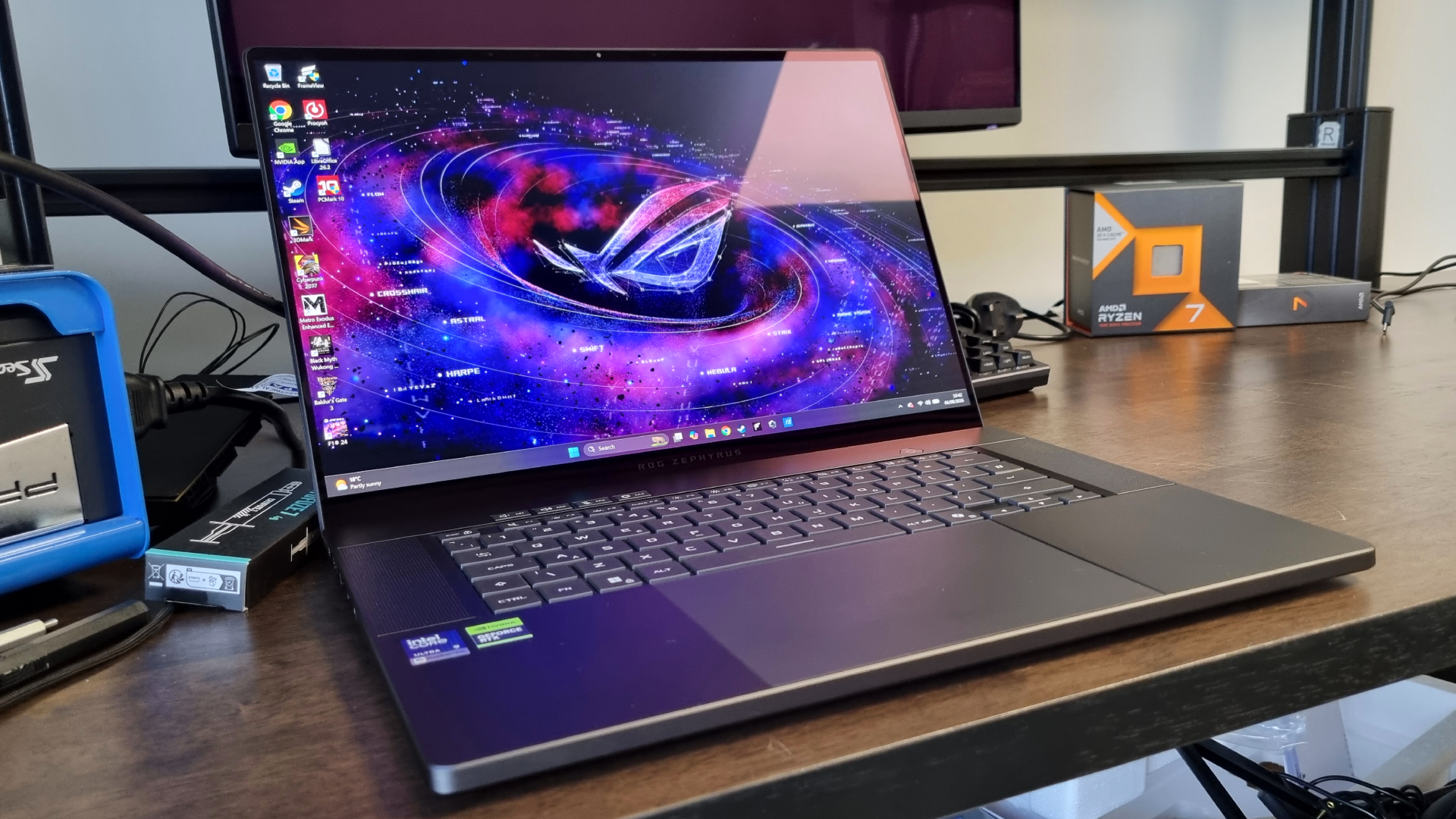 An Asus ROG Zephyrus G16 gaming laptop next to a benchmarking rig