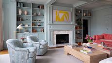 Pale blue living room with built in shelving and a bright coral sofa