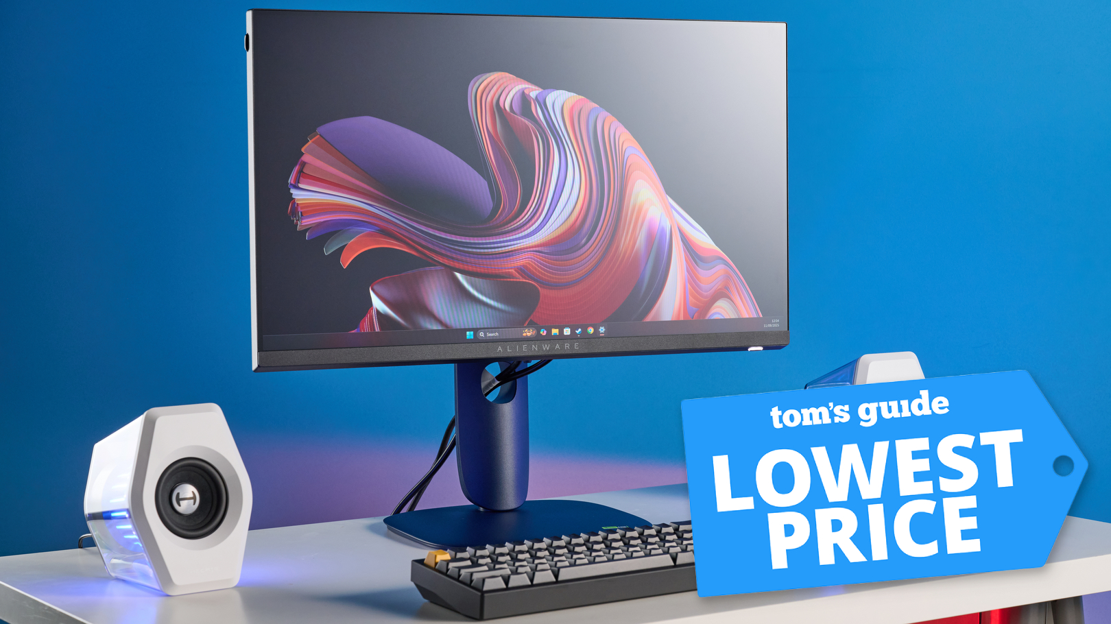 Alienware AW2525HM on desk with speakers and keyboard with Tom&#039;s Guide Lowest Price badge