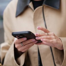 woman wearing beige trench and holding mobile phone with milky pink manicure 