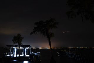 A perseid meteor passing over bright lights next to a large lake.