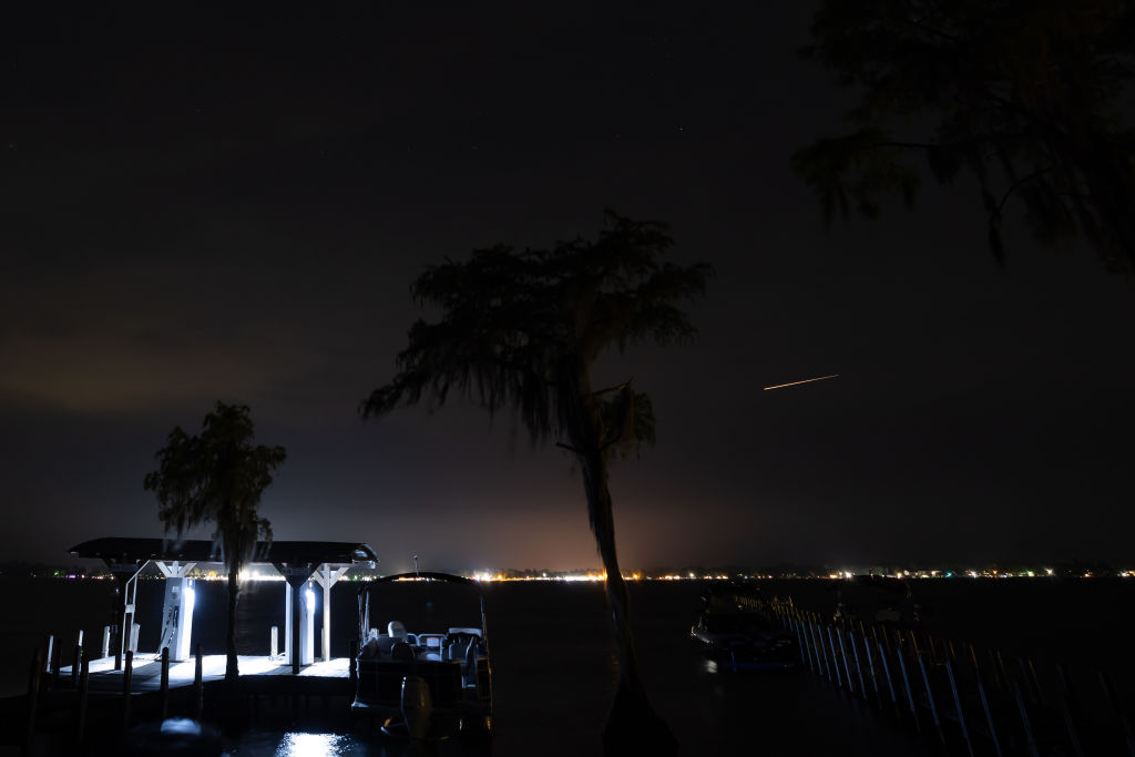 Una meteora prominente passa sopra luci brillanti accanto a un grande lago.