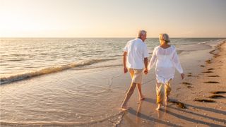 An older couple walk toward the sunset on the beach.
