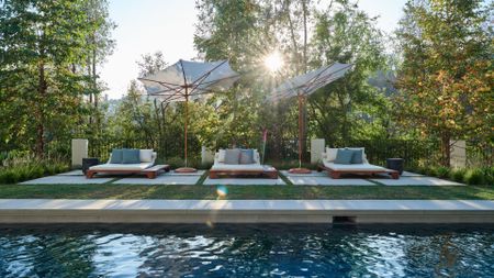 A backyard with a pool and three sun loungers under two large parasols